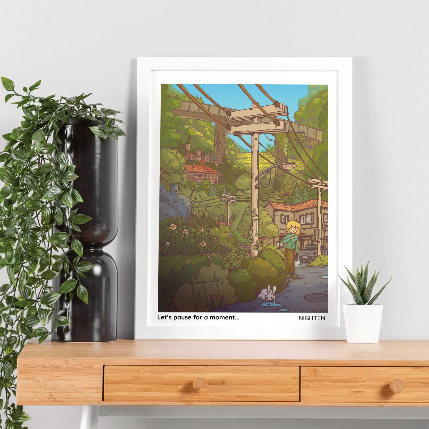 Framed artwork of a scenic landscape with a character and text, displayed on a wooden shelf with plants.