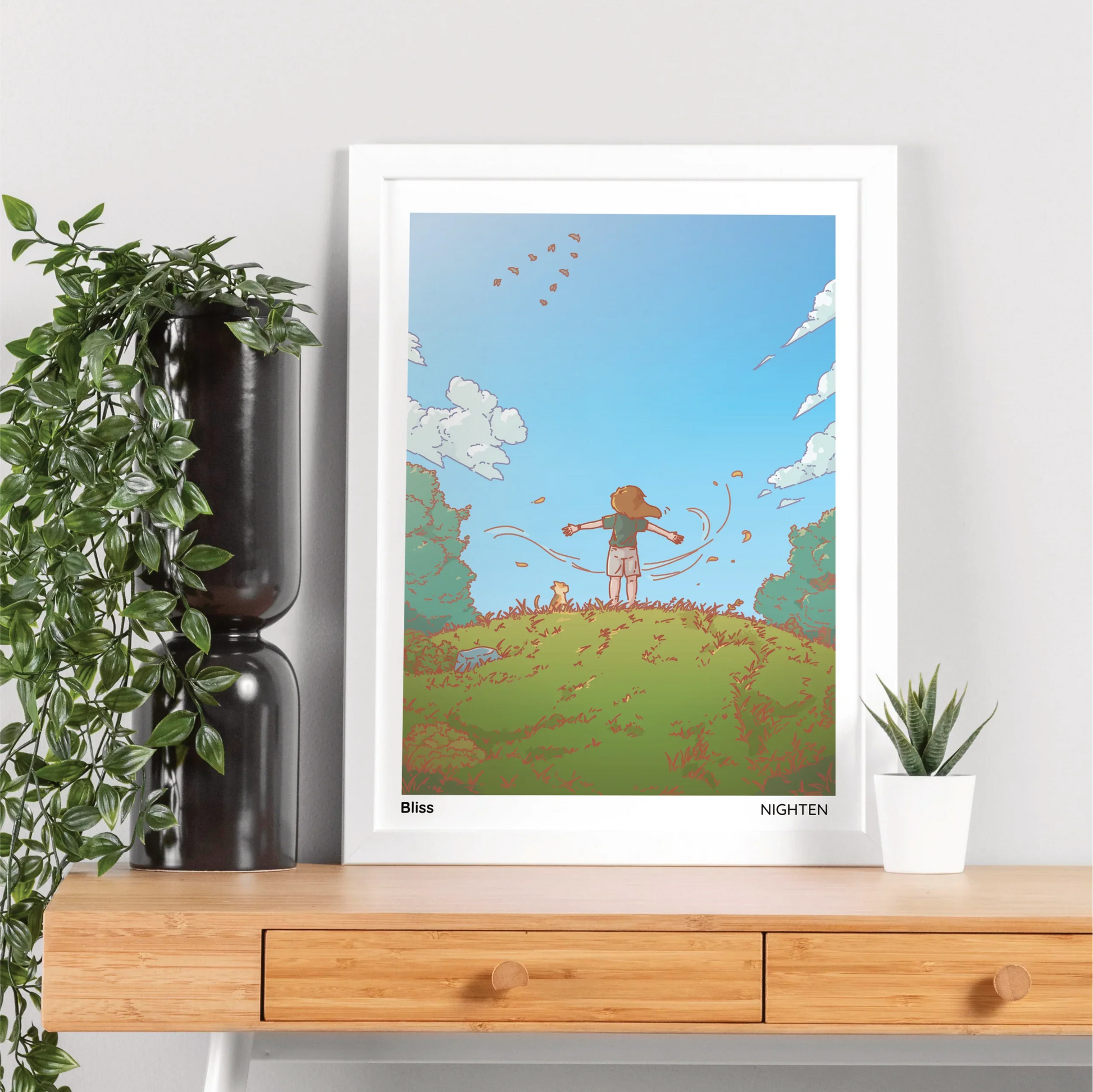 Framed artwork of a person standing serene on top on a hill. The frame is on a wooden shelf with plants.